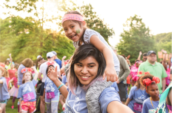 A Girls on the Run 5K participant smiles while holding a smaller child on her shoulders